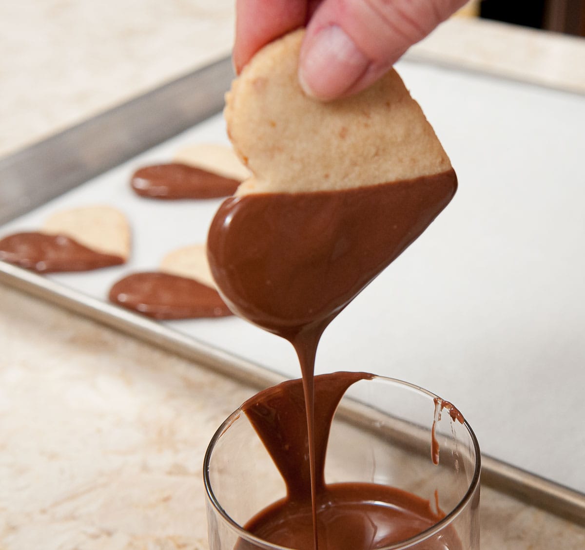 The back of the cookie is being lightly wiped on the rim of the glass to remove chocolate that would puddle around the bottom of the cookie.