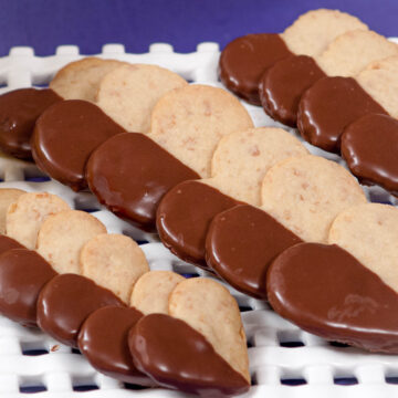 Tropical Shortbreads half dipped in chocolate on a lattice platter in front of a purple background.