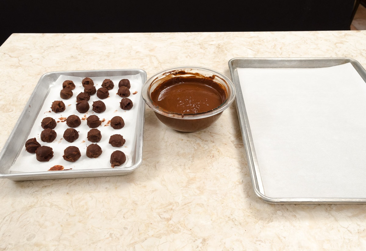 The set up to coat the chocolate from left to right is a tray of chocolate centers, the meited chocolate and a tray lined with parchment paper.