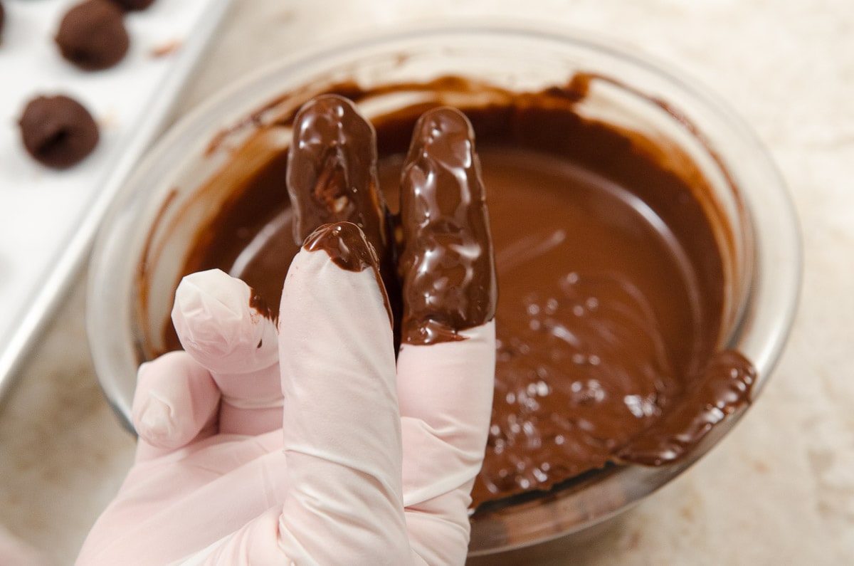 A gloved hand with two fingers dipped in chocolate