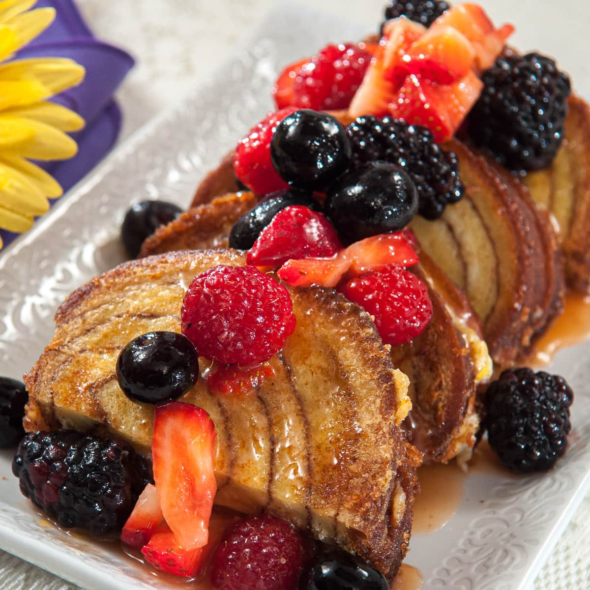 Slices of the French Toast with the Orange Cream Sauce fruit on a white plate with a bit of a yellow daisy and purple napkin.