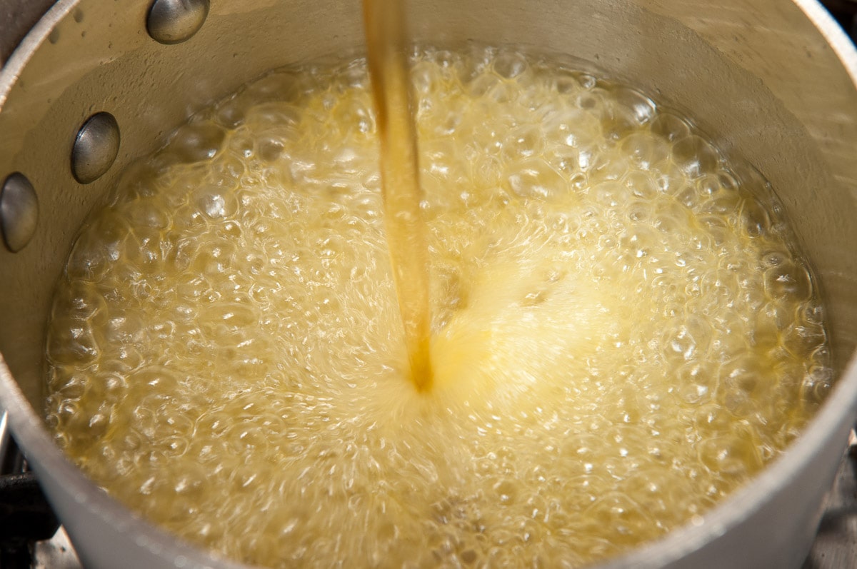 Orange liqueur and brandy being poured into the pan with the boiling syrup.