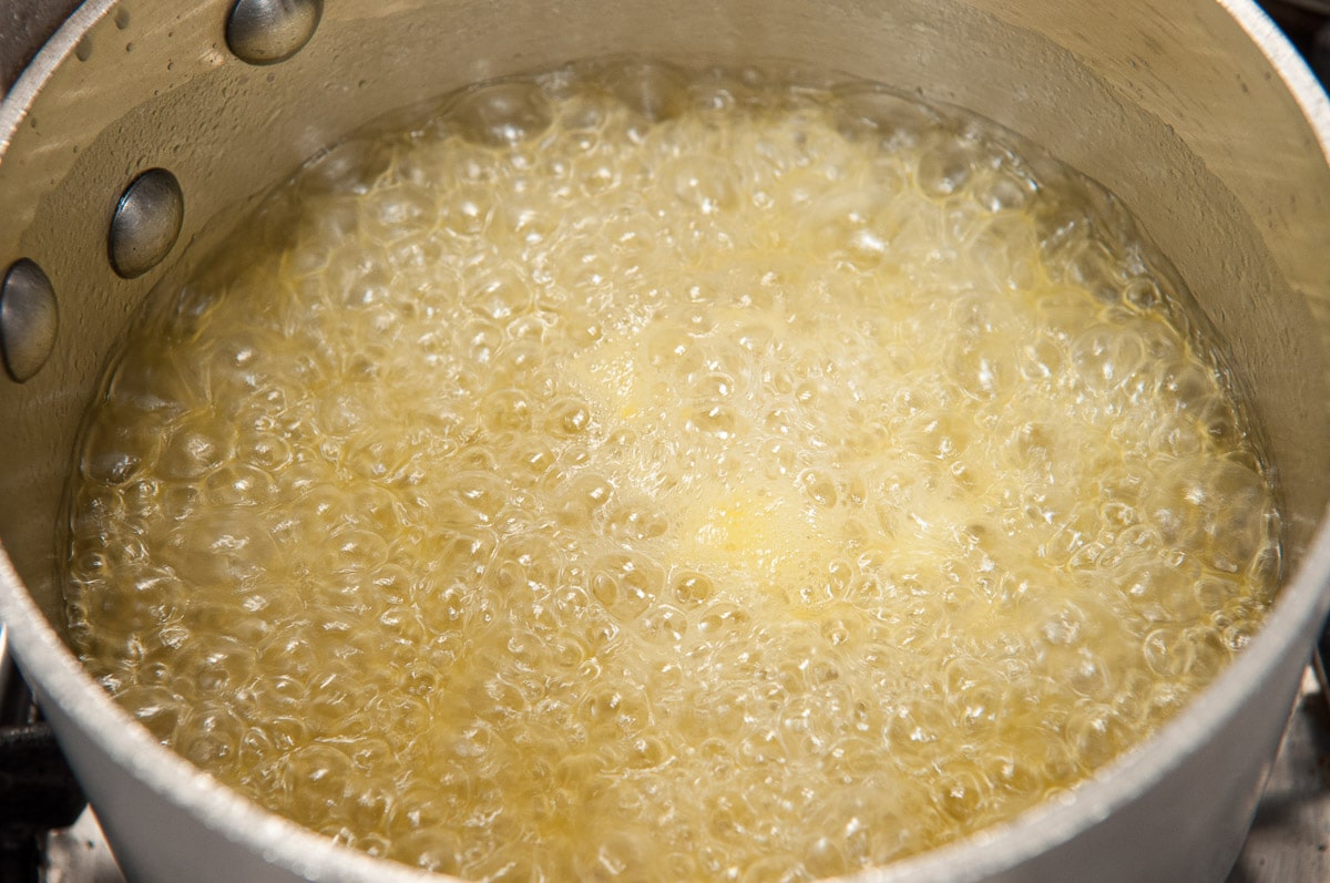 The sauce is boiling really hard with large bubbles covering the entire pot.
