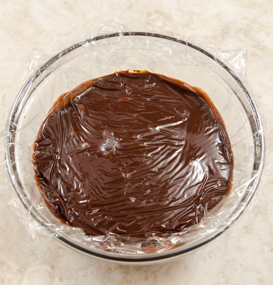 The chocolate truffle mixture is transferred to a bowl and covered with plastic wrap to cool.