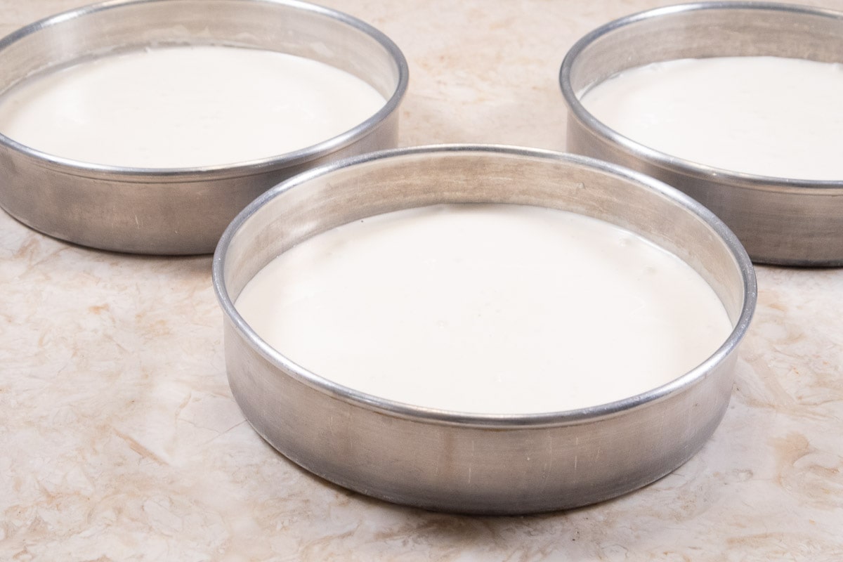 The finished cake batter is divided between three pans.