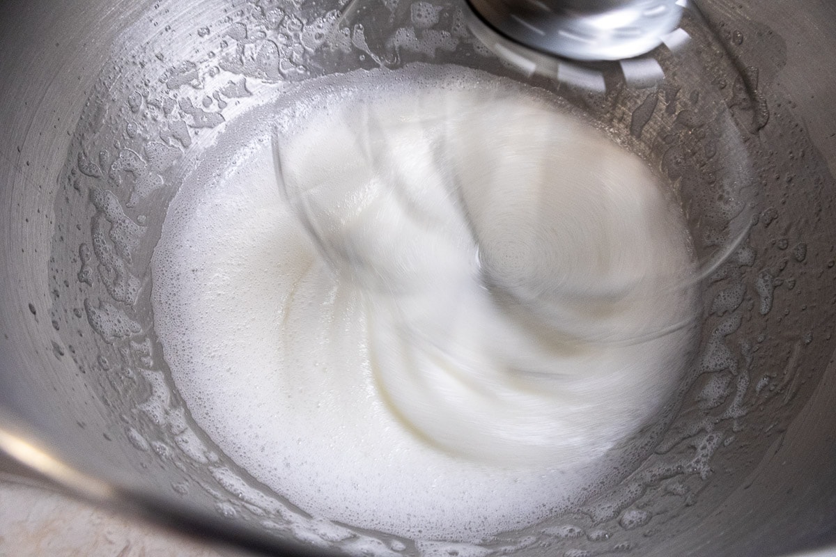The egg whites are being whipped in the bowl with the whisk leaving a trail in them.