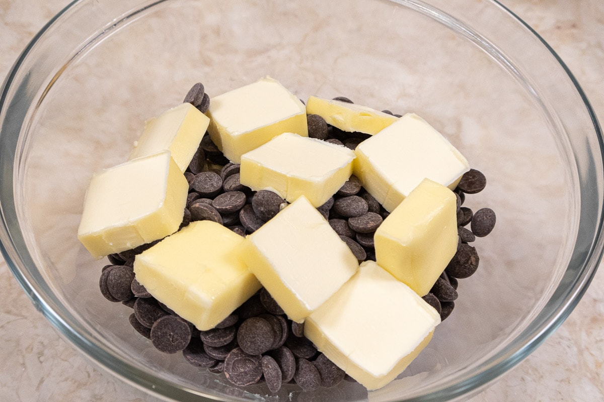 The butter is cut into small pats and combined in a bowl with the chocolate.