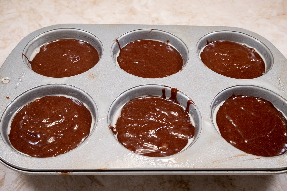 The chocolate batter is divided between six Texas muffin cups.
