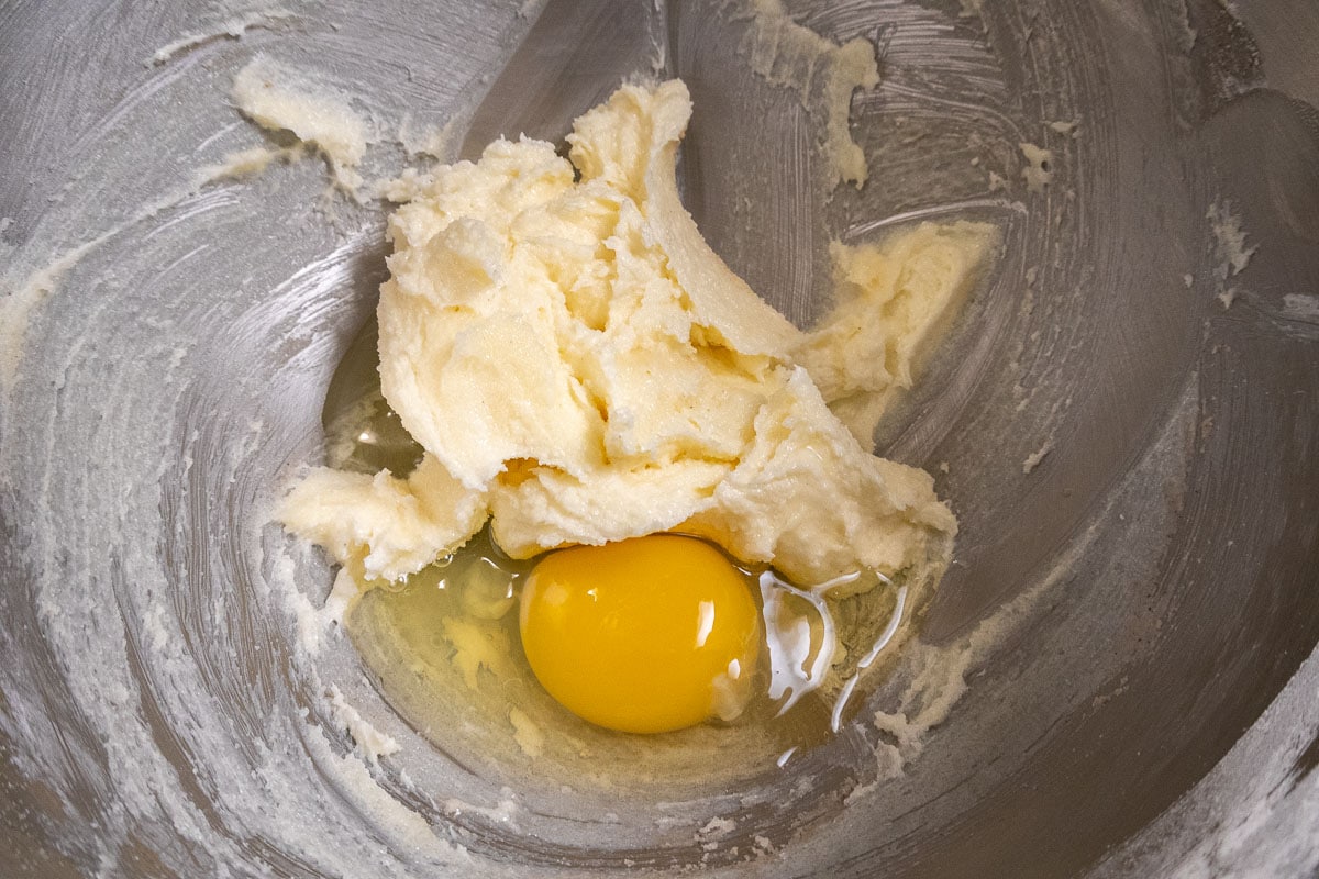 One egg is added to the creamed mixture in the bowl.