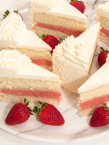 Slices of the Strawberry Cake sit on a marble plate with fresh strawberries.