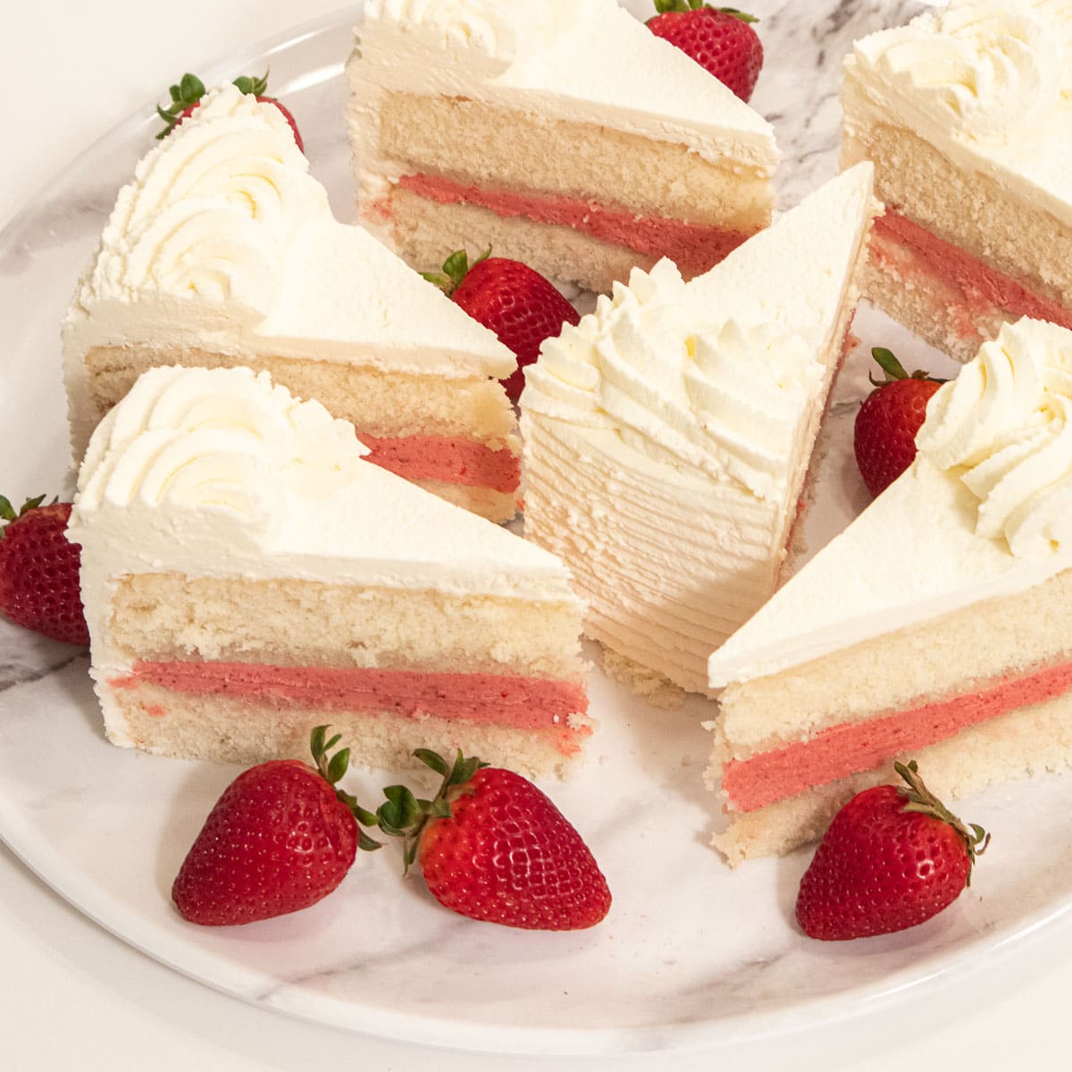 Slices of the Strawberry Cake sit on a marble plate with fresh strawberries.