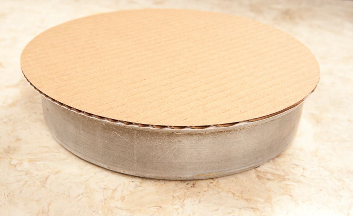A cake board is placed on top of the cake pan,