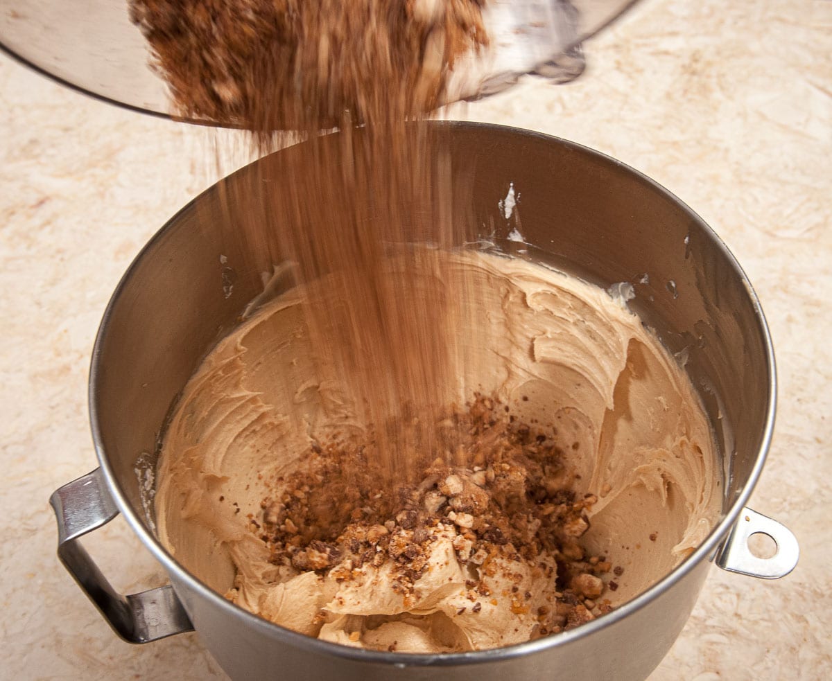 Pouring the snickers pieces into the mousse mixture in the mixer.