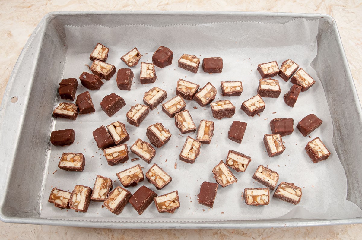 The cut Snickers are placed on a parchment lined tray to be placed in the freezer.