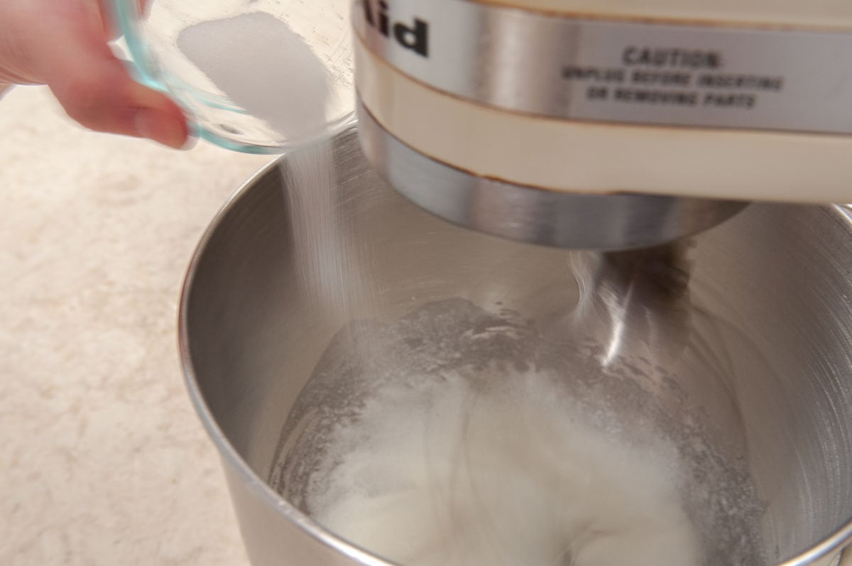 The sugar is being added slowly to the beating egg whites in the mixing bowl.