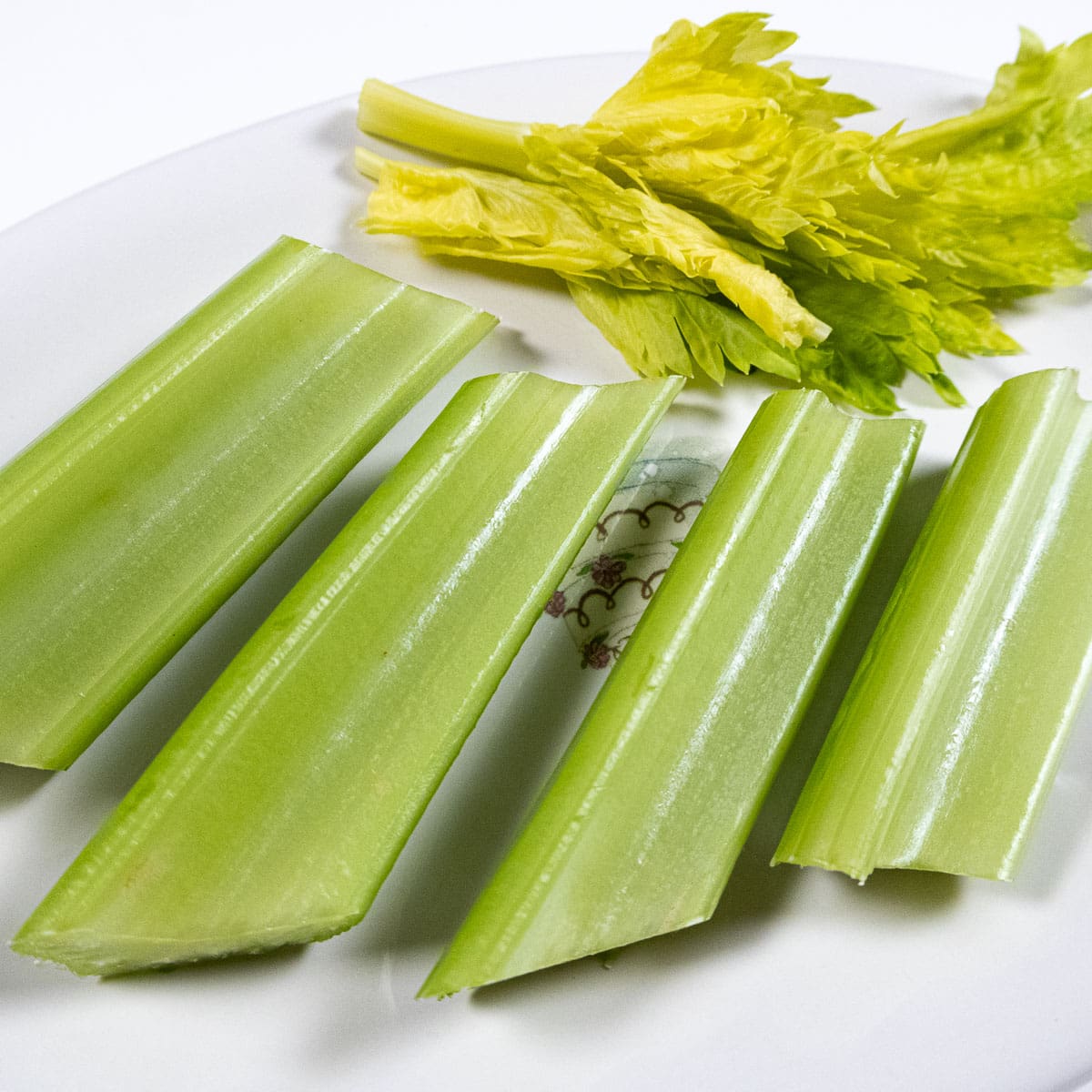4 pieces of celery with celery leaves on a plate.
