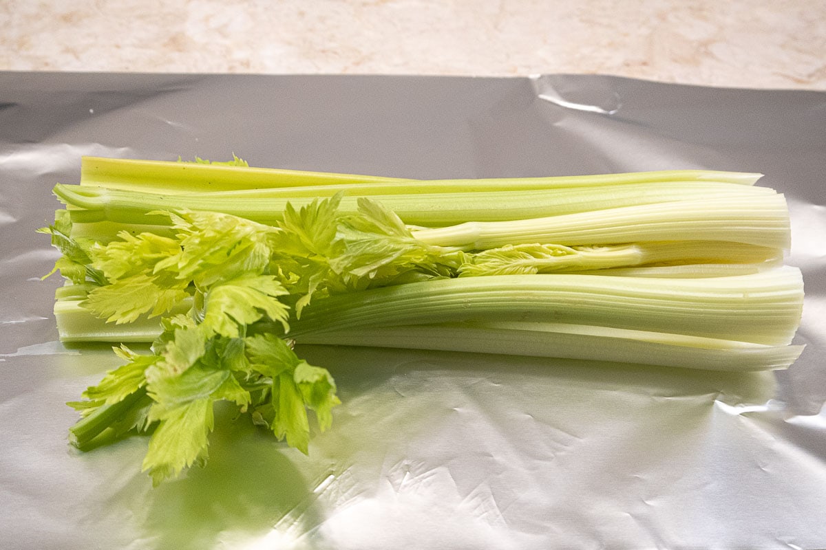 Celery, with its top and bottom cut off lays on a large piece of foil.