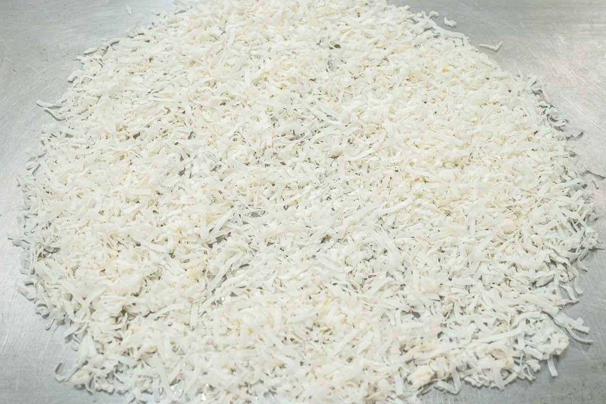 Unsweetened coconut is spread in a single layer on a baking sheet.