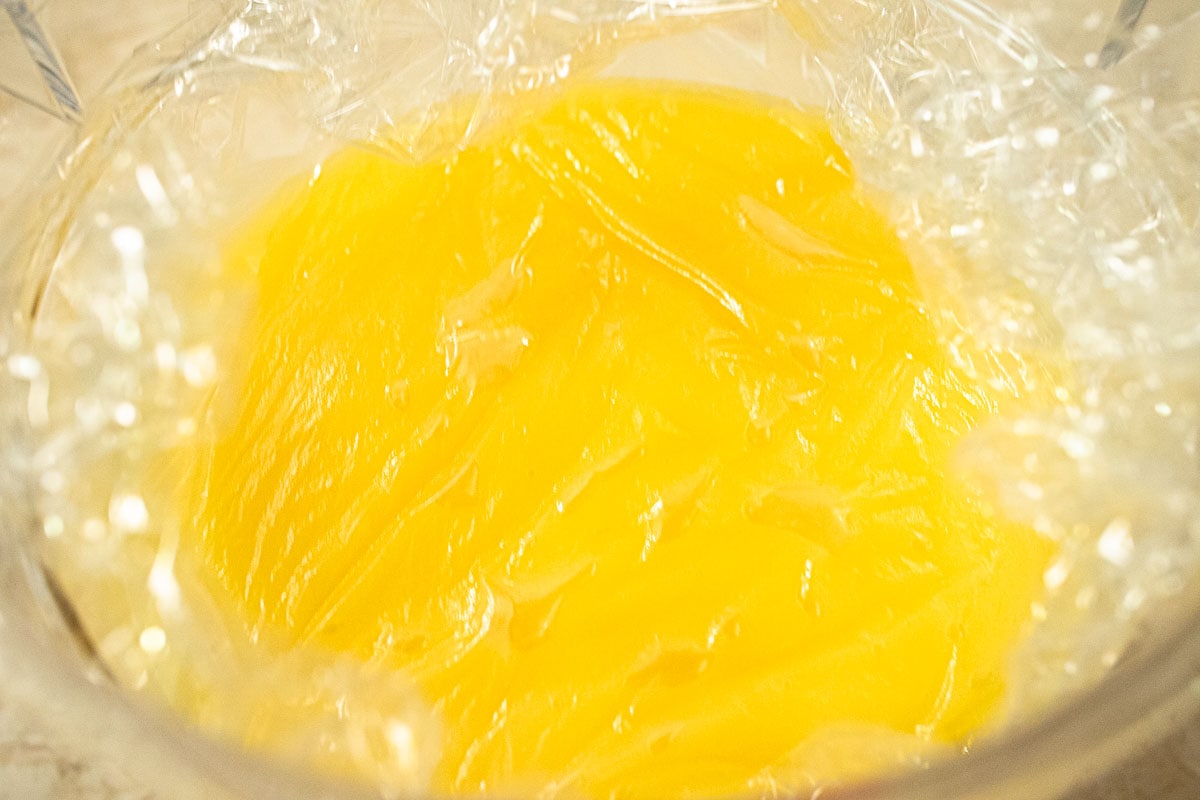 The curd is poured in a storage container and the top of the curd is covered with plastic wrap.