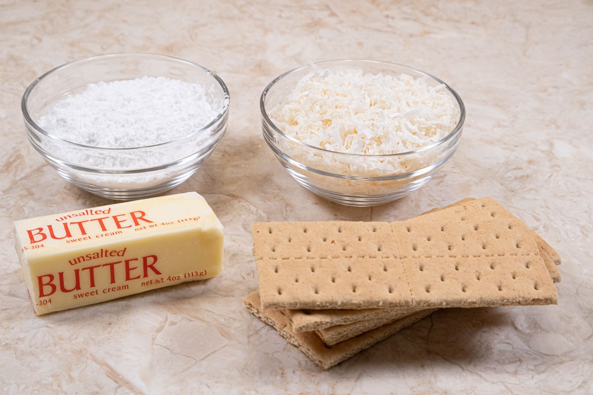 The ingredients for the cheesecake crust are powdered sugar, unsweetened coconut, unsalted butter and graham crackers.