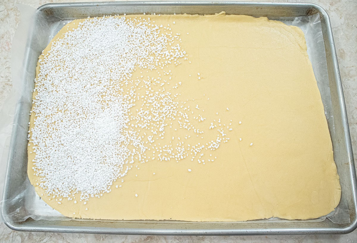 Dough rolled out and placed in a half sheet pan.  Swedish pearl sugar covers about ⅓ of it.