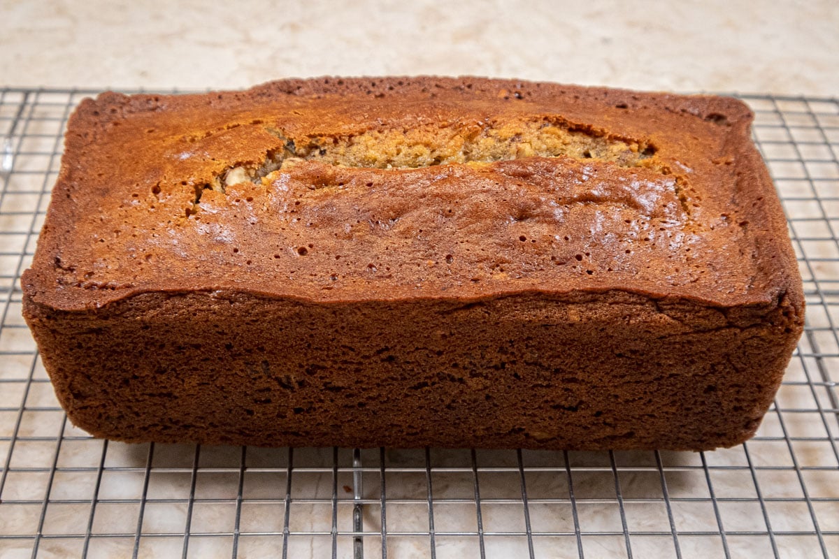 The loaf of baked banana bread sits on a cooling rack.