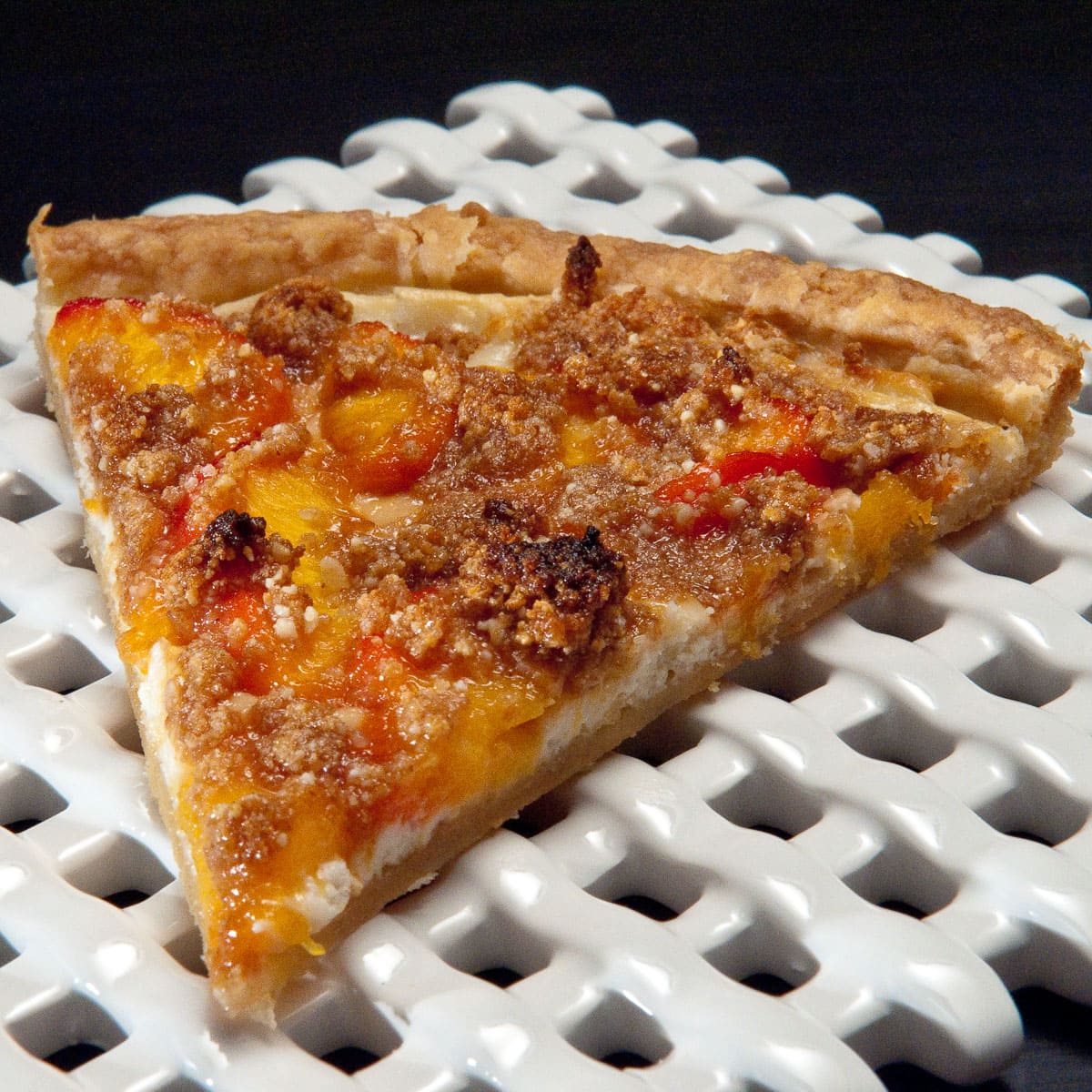 A slice of Peach Pizza sits on a white lattice tray on a black background.