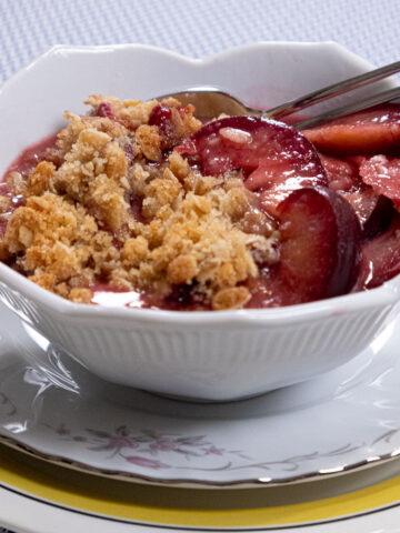 Plum Crisp ready to eat with a spoon in a white bowl.