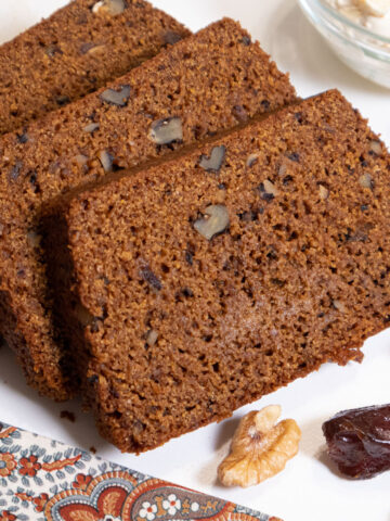 Slices of Date Nut Bread on a plate with walnut halves and dates around it.