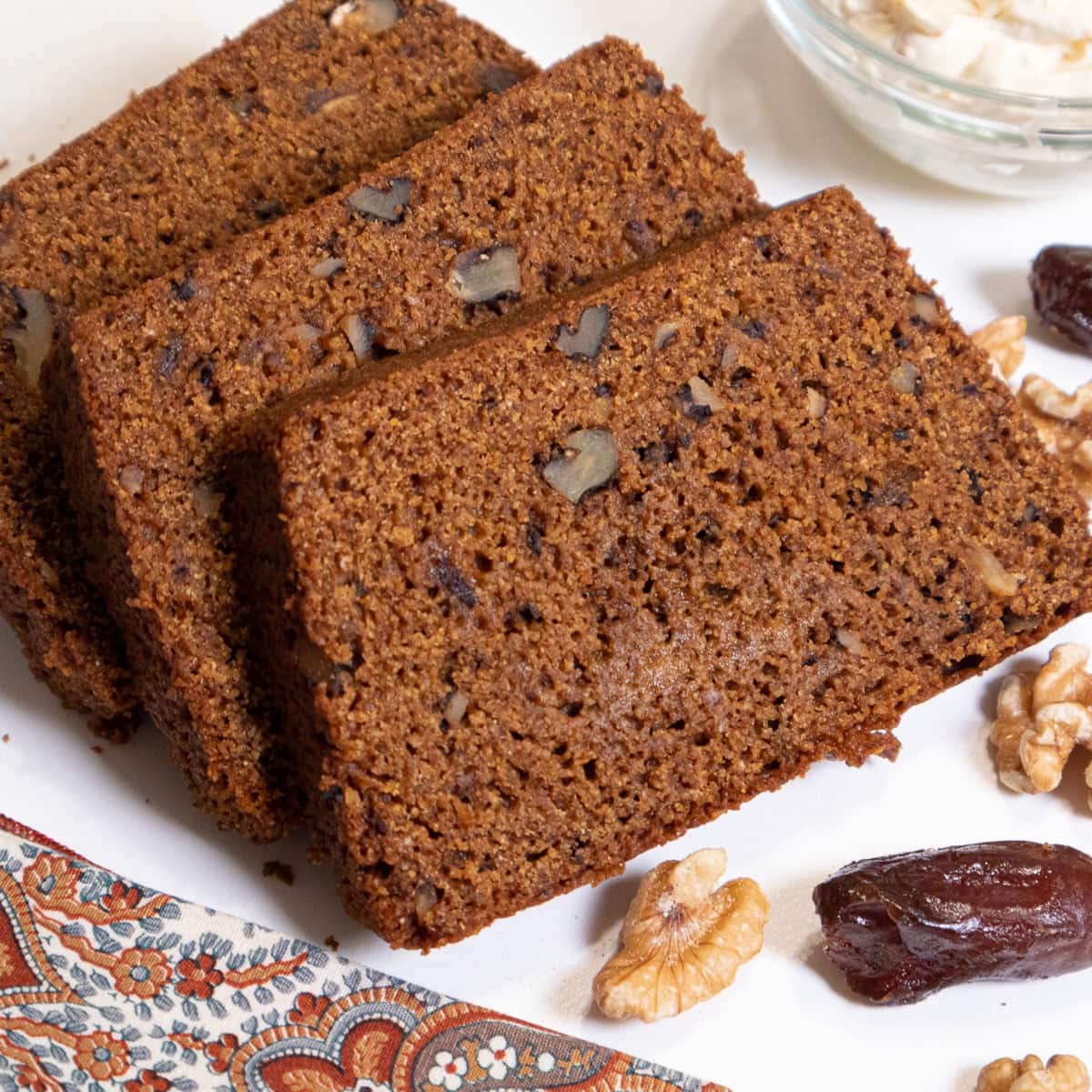 Slices of Date Nut Bread on a plate with walnut halves and dates around it.  