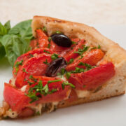 A slice of the French Onion Tart showing the tomatoes and olives in the yeasted crust with a sprig of basil.