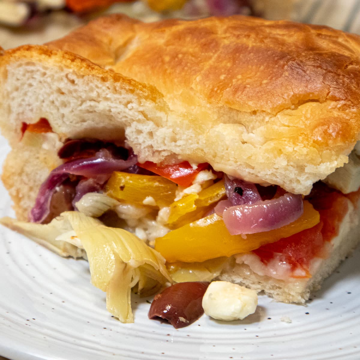 A slice of Stuffed Focaccia over flowing with vegetables.