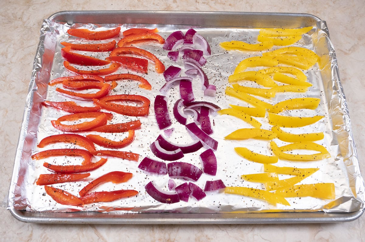 Red and yellow pepers as well as red onions, cut and seasoned before roasting.