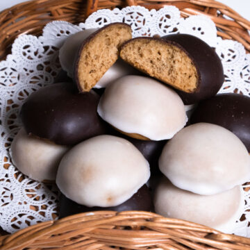 A wicker basket with a doilie holds black and white glazed Pryaniki cookies.