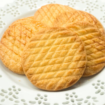 Round Sable Breton cookies that are cross hatched on a lace edged plate.