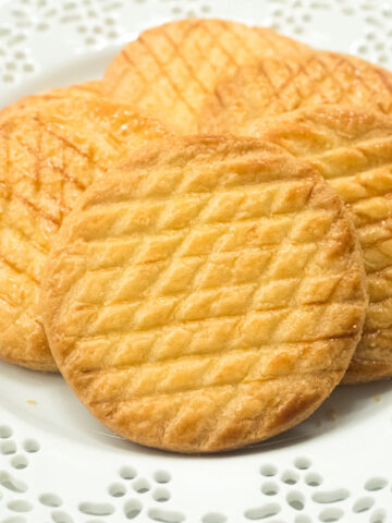 Round Sable Breton cookies that are cross hatched on a lace edged plate.