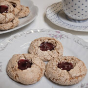 A plate of 3 Haselnussmakronen -German Hazelnut Macroons on a plate with a cup and saucer and more macaroons in the background.