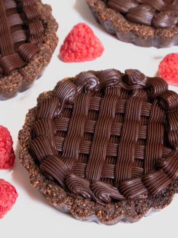 An individual Chocolate Caramel Tart on a white background with raspberries.