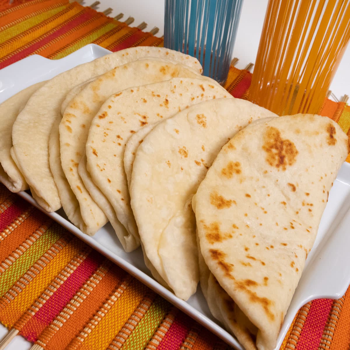 This final photo shows the flatbreads folded up on a white tray placed on a colorful runner with 2 glasses in the background.