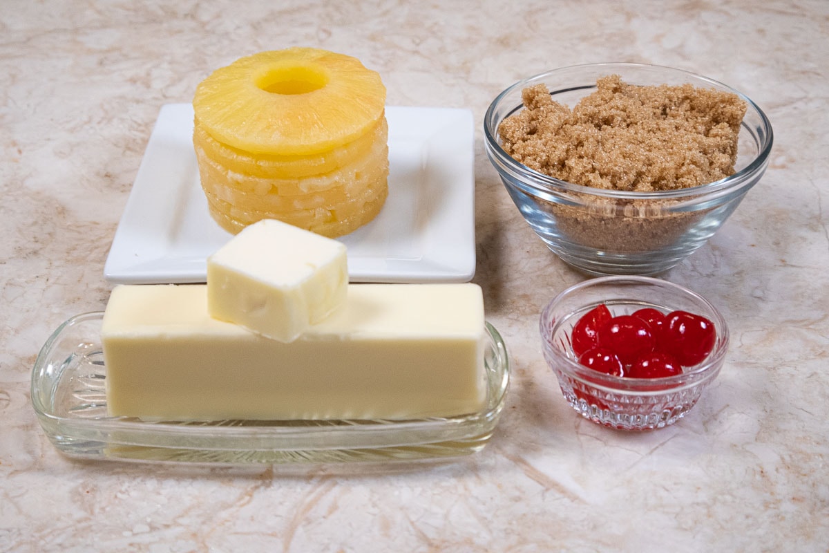 The ingredients for the pineapple layer are canned pineapple slices, brown sugar, butter and marachino cherries.