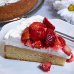 A slice of the gluten free Lemon Strawberry Cake sits on a white plate with daisies on the table.