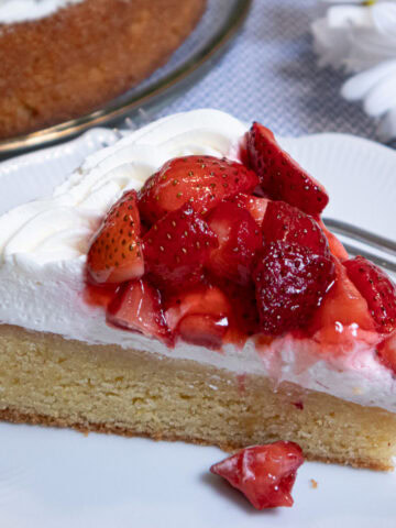 A slice of the gluten free Lemon Strawberry Cake sits on a white plate with daisies on the table.