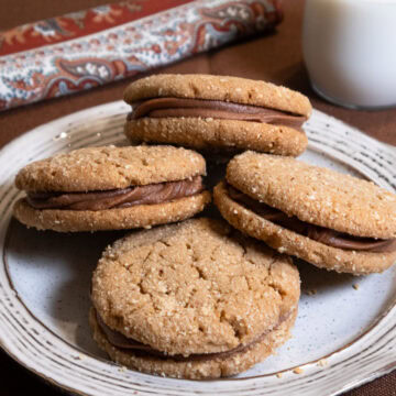 Four Peanut Butter Sandwich Cookies on a white plate with a brown rim.