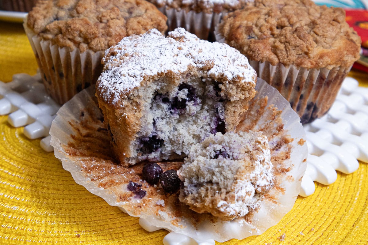 This photo shows a muffin, topped with powdered sugar broken open in its paper liner.