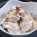Scoops of Caramel Brickle ice cream in a white dish on a gray plate.