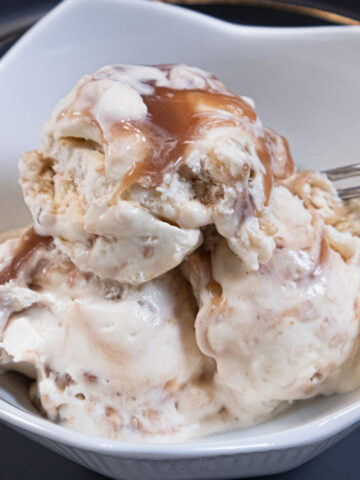 Scoops of Caramel Brickle ice cream in a white dish on a gray plate.