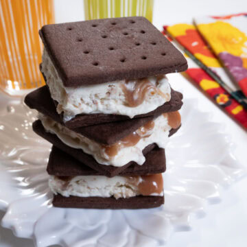 Three Ice Cream Sandwiches on a white plate with multi colored glasses and napkins behind.