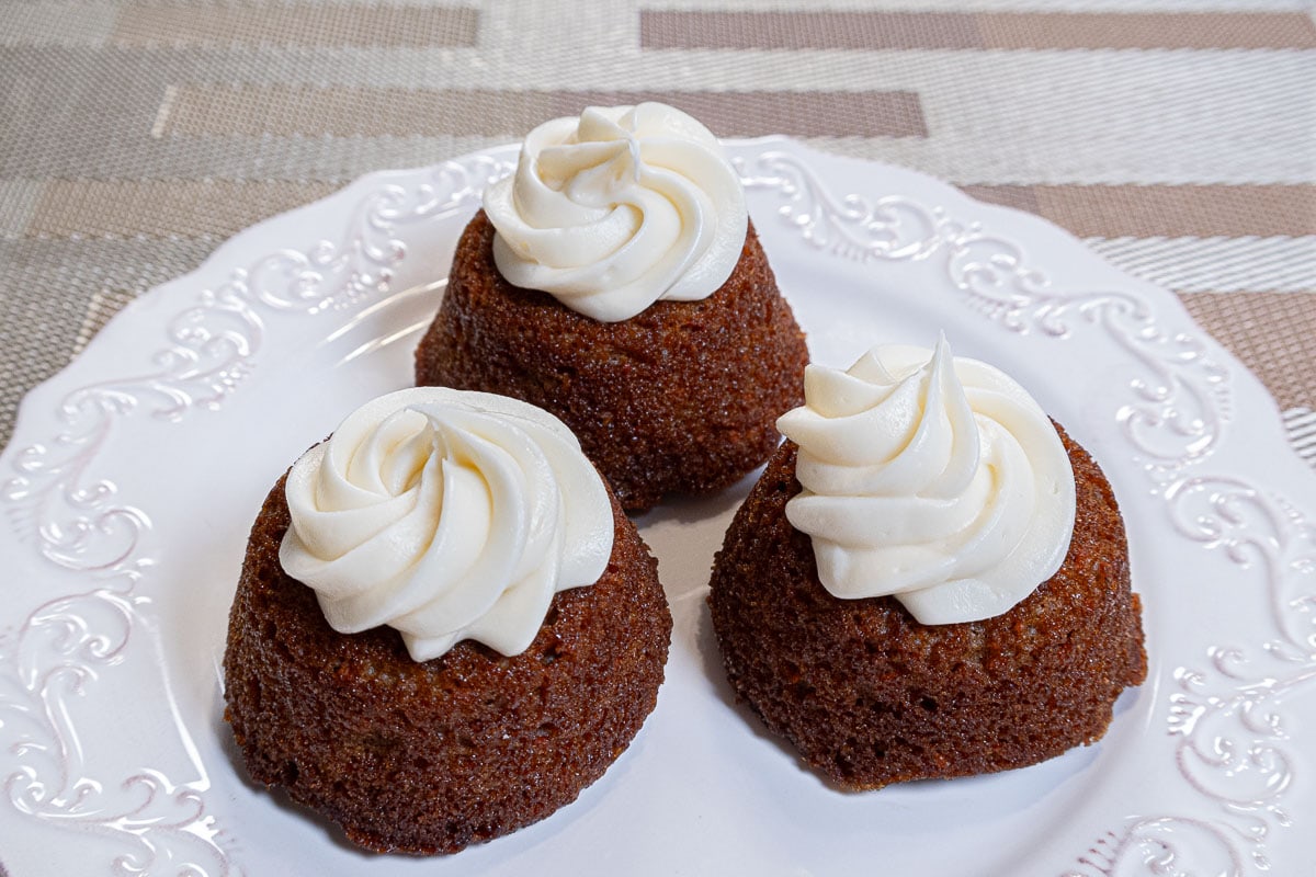 This photo shows three carrot cake baked doughnuts in muffin tins finished with swirls of  cream cheese frosting. 