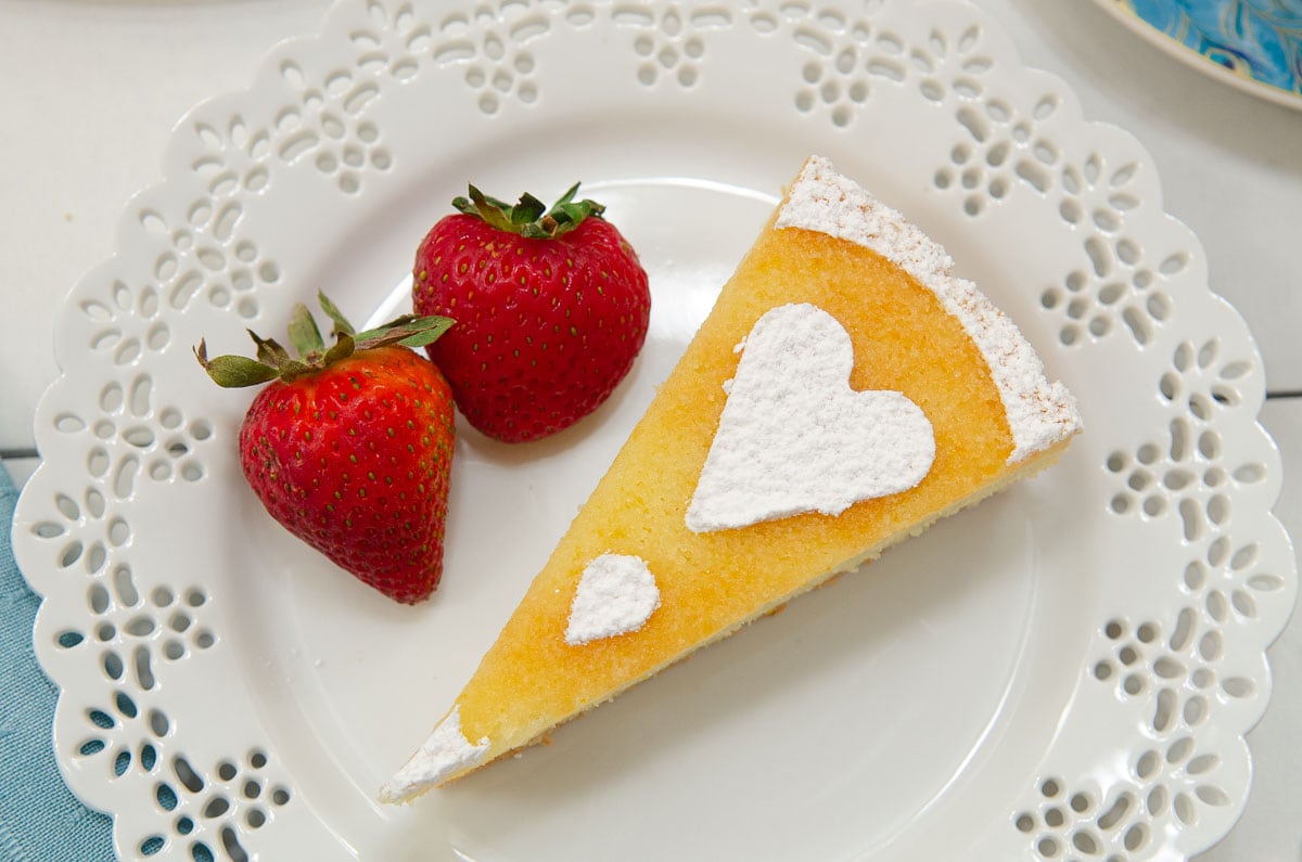 This phots is a down shot of the tart on a lace edged white plate with 2 red strawberries.