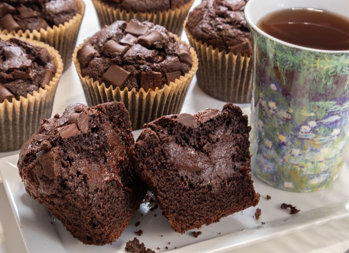 This picture shows the the muffin cut in half with a cup of tea next to it and more muffins in the background.